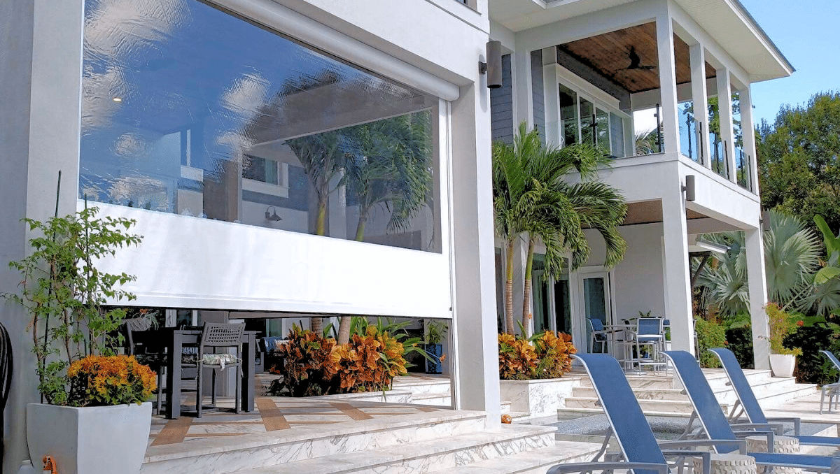 Motorized vinyl porch enclosure panel partially lowered on a luxury outdoor patio, creating a protected outdoor living space while maintaining views.