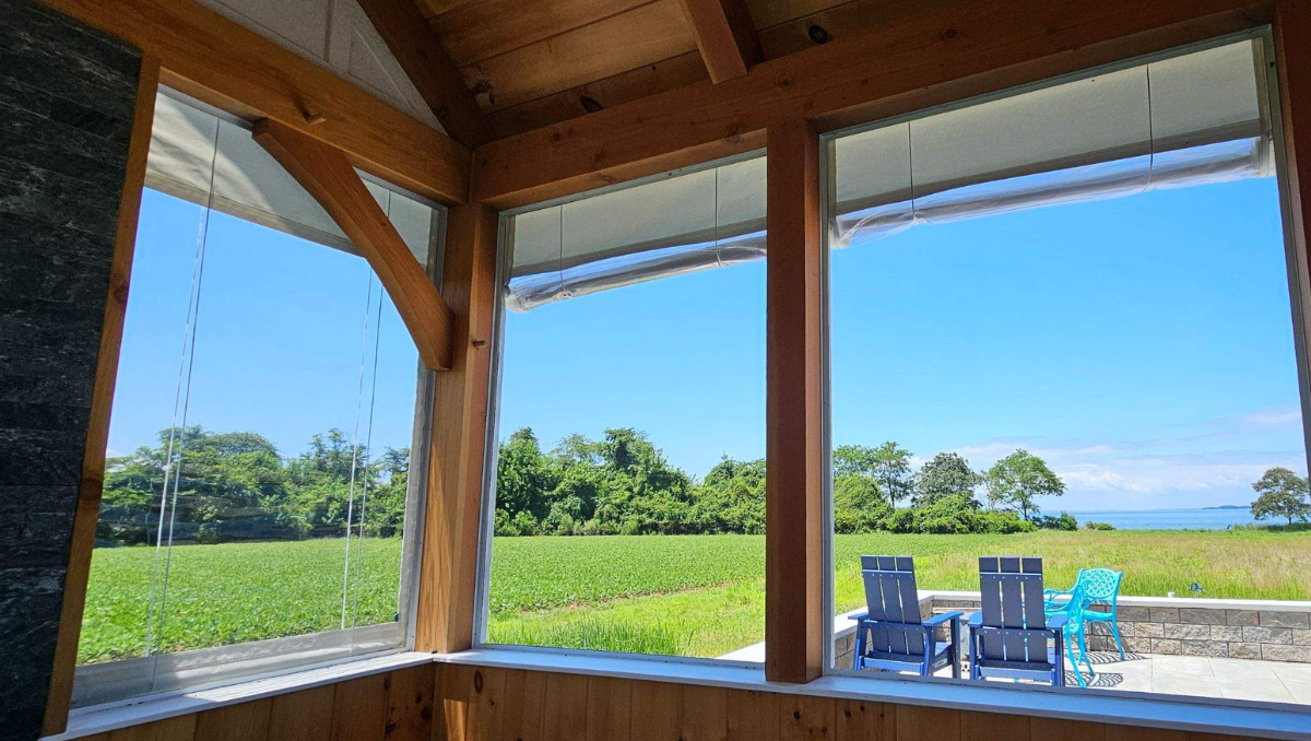 Manual vinyl porch enclosure panels rolled up on a coastal porch overlooking farmland and water on the Eastern Shore.