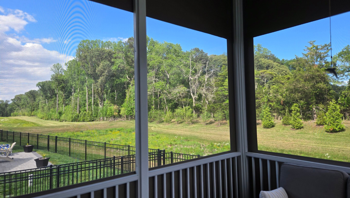 View from inside a vinyl porch enclosure overlooking a wooded landscape through crystal-clear vinyl panels