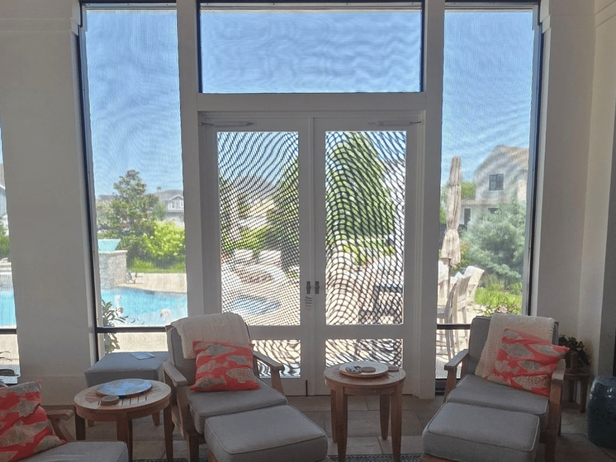 View from inside the home looking through motorized solar privacy screens toward the swimming pool.