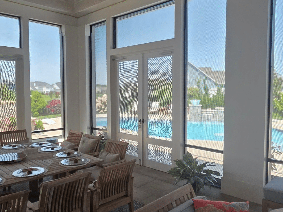 Dining area overlooking a swimming pool through motorized solar screens in Lewes, Delaware.