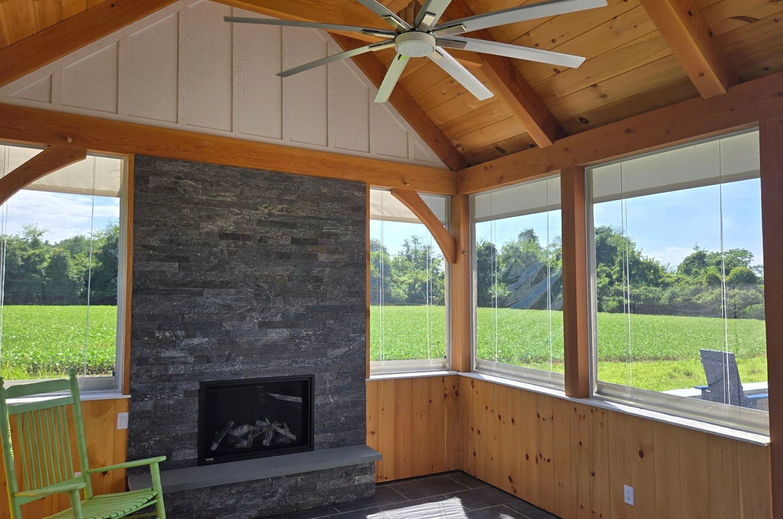 Covered timber-frame porch with a stone fireplace and motorized porch screens overlooking the countryside.