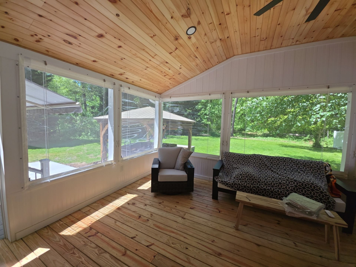 Bright enclosed porch fitted with clear vinyl panels overlooking a landscaped backyard.