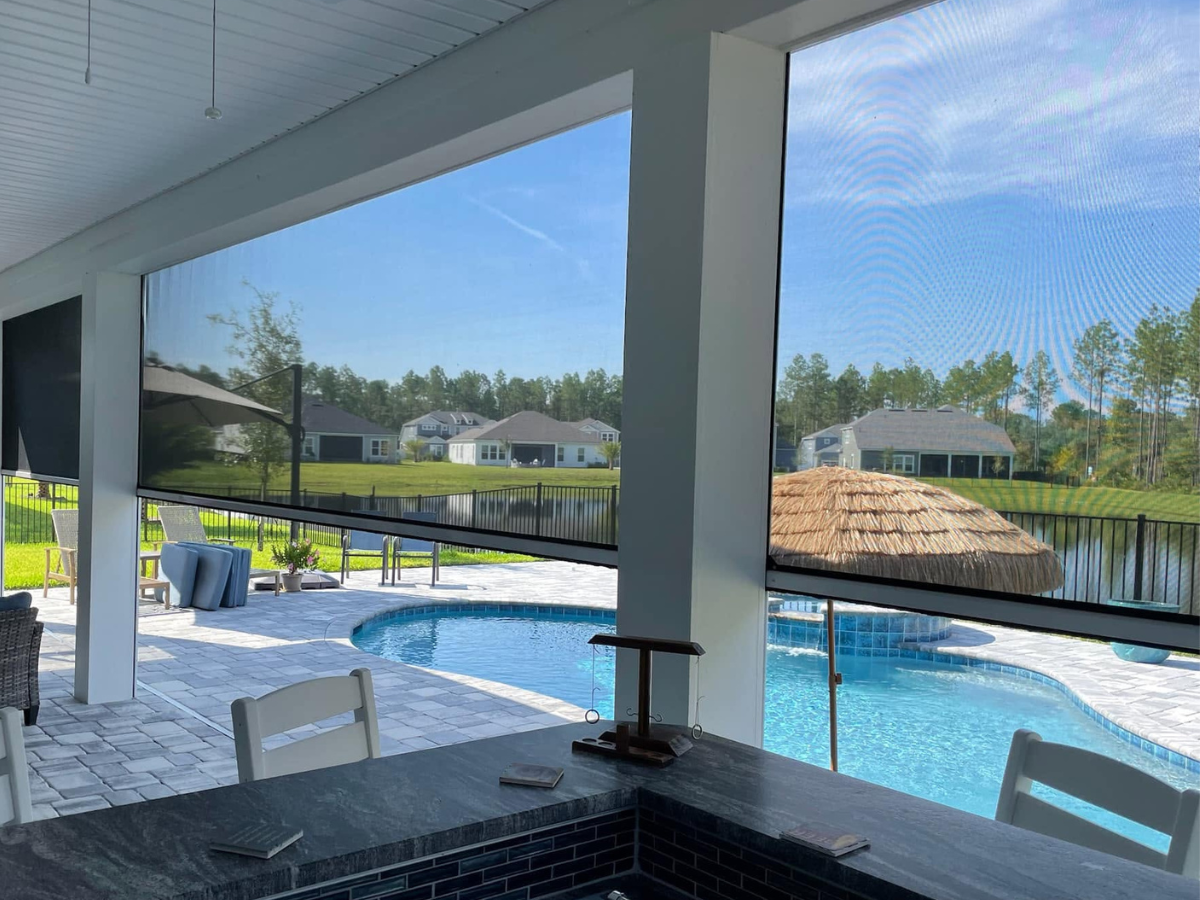 Outdoor kitchen overlooking a swimming pool protected by motorized porch screens for shade and insect control.
